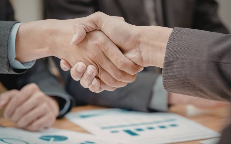 Borrower and lender shaking hands over financial documents after agreeing on loan terms